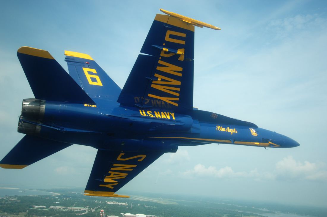 Blue and gold Blue Angels jet banking over Naval Air Station Pensacola with coastline below